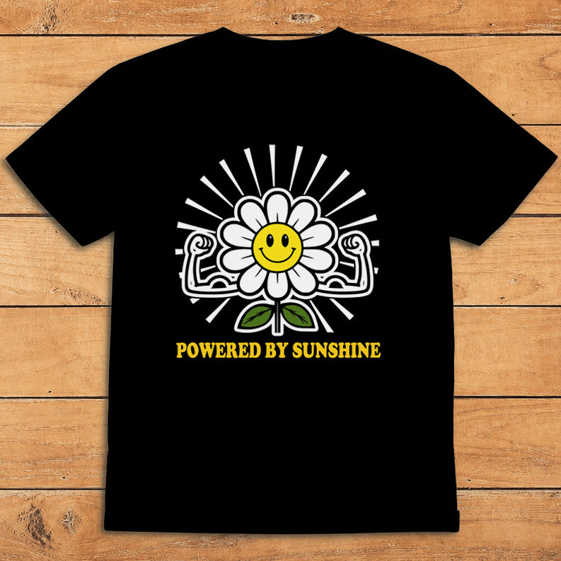 Black sunshine T-shirt featuring a smiling daisy flexing its arms and the words “Powered by Sunshine”