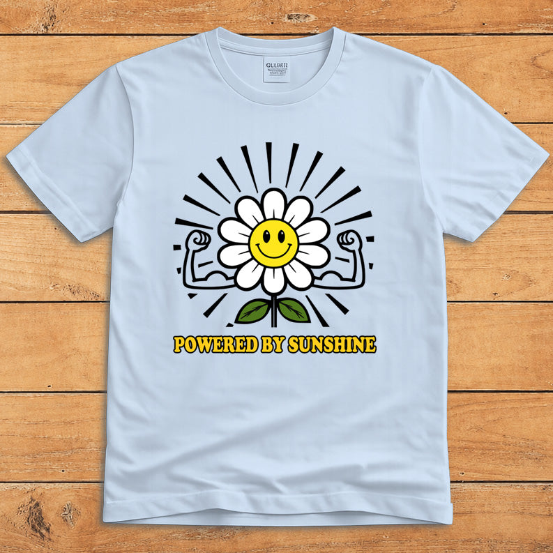 Light blue sunshine T-shirt featuring a smiling daisy flexing its arms and the words “Powered by Sunshine”